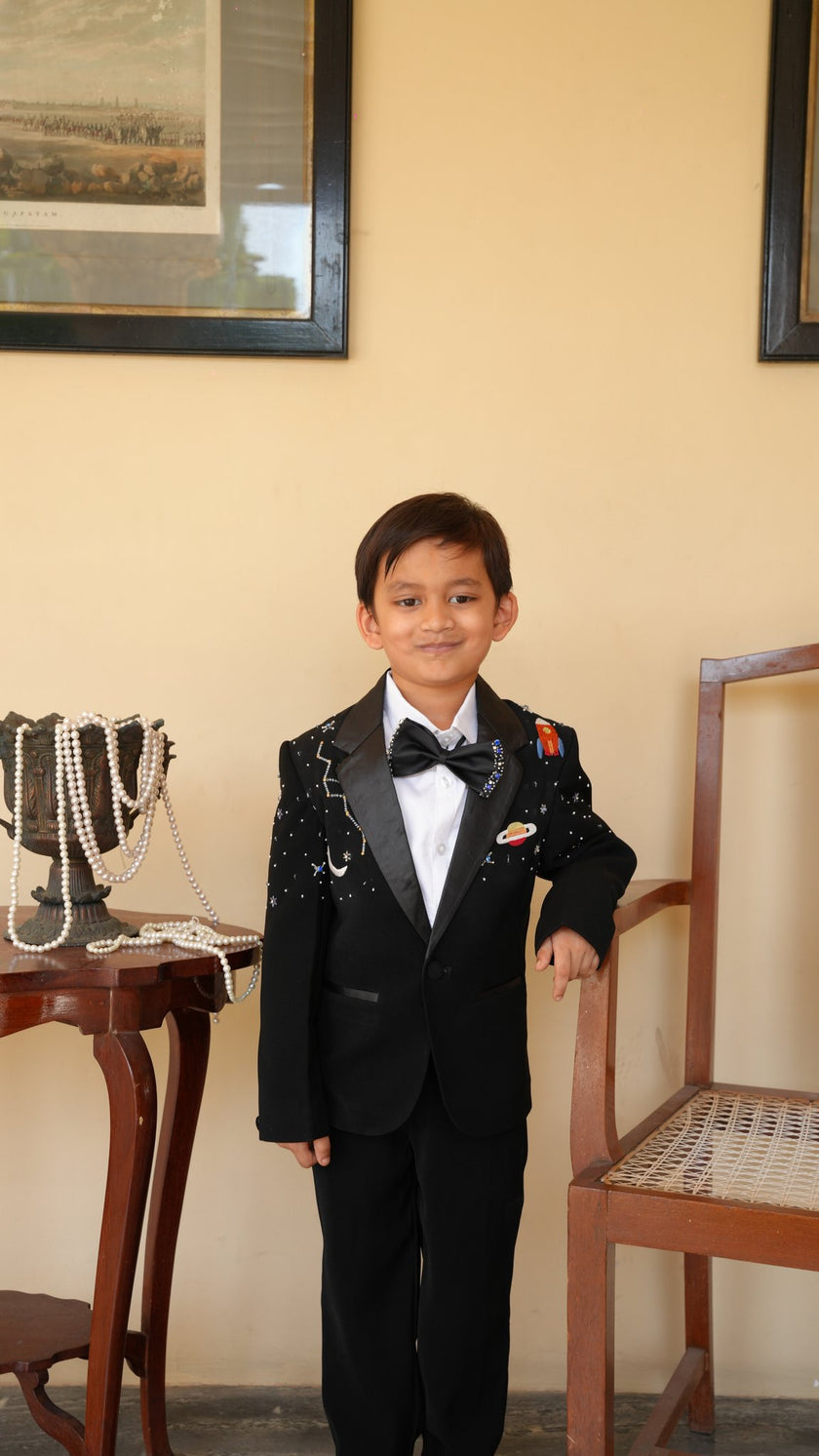 FunnyBones Black Tuxedo with Galaxy Embroidery – boy posing by a chair
