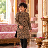 Smiling boy walking in the FunnyBones camel brown achkan with black floral embroidery and black velvet buttons, with black suiting pants