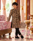 Boy leaning on a palace sofa in the long-line camel brown embroidered achkan and black pants