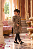 Boy smiling over his shoulder in the knee-length camel brown floral embroidered achkan set