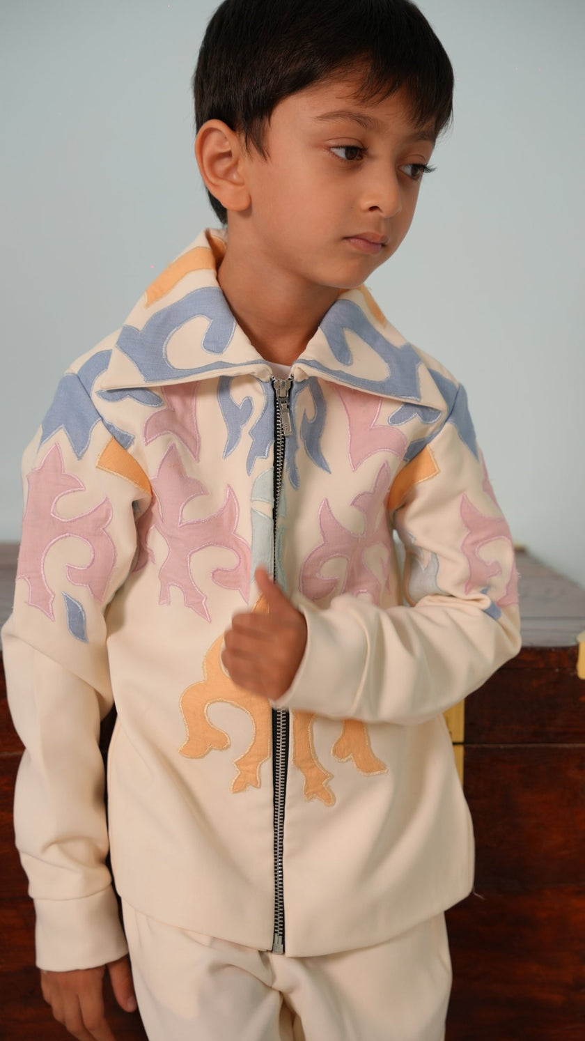 Boy wearing the FunnyBones Mesmerising Colours ivory zipper jacket with pastel blue, pink and peach appliqué and a spread collar, with matching ivory pants