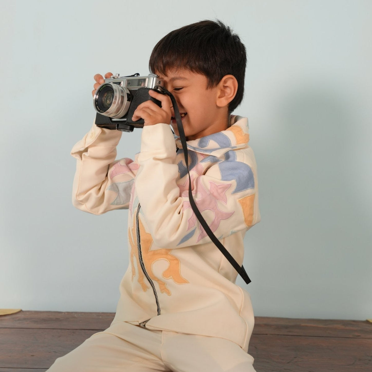 Boy in the ivory zipper jacket set with pastel appliqué, smiling while taking a photo with a vintage camera