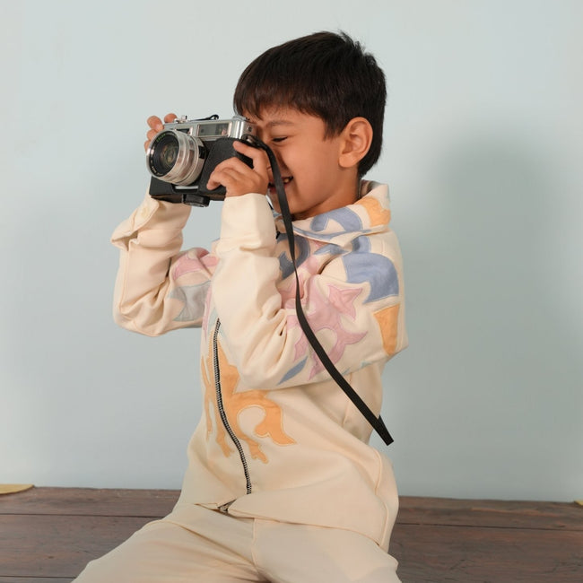 Boy in the ivory zipper jacket set with pastel appliqué, smiling while taking a photo with a vintage camera