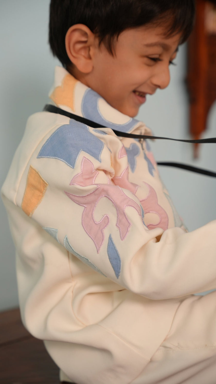 Side view of the ivory zipper jacket sleeve showing pastel pink, blue and peach appliqué motifs