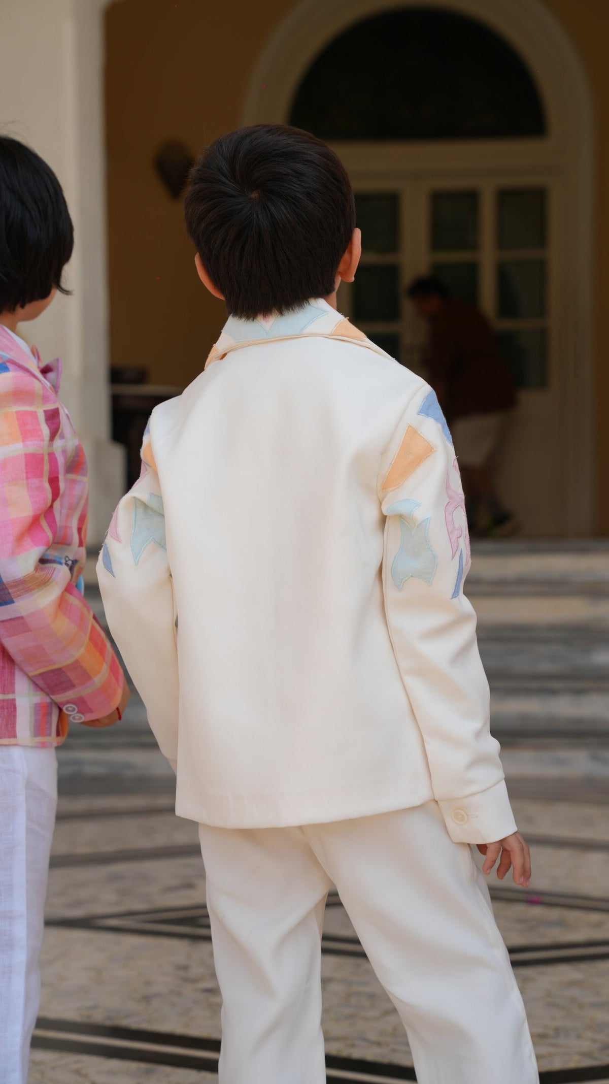 Back view of the ivory zipper jacket with pastel appliqué on the collar and sleeves, worn with ivory pants
